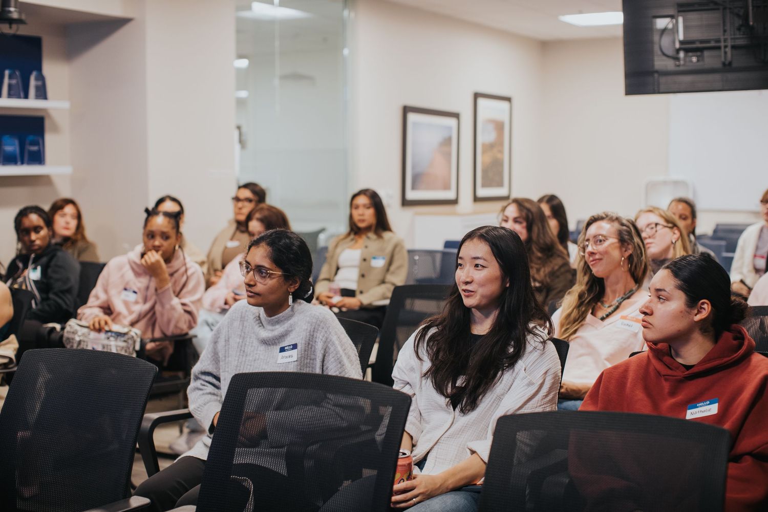 Diverse group of young women smiling and engaged in a presentation at an indoor professional event or workshop.