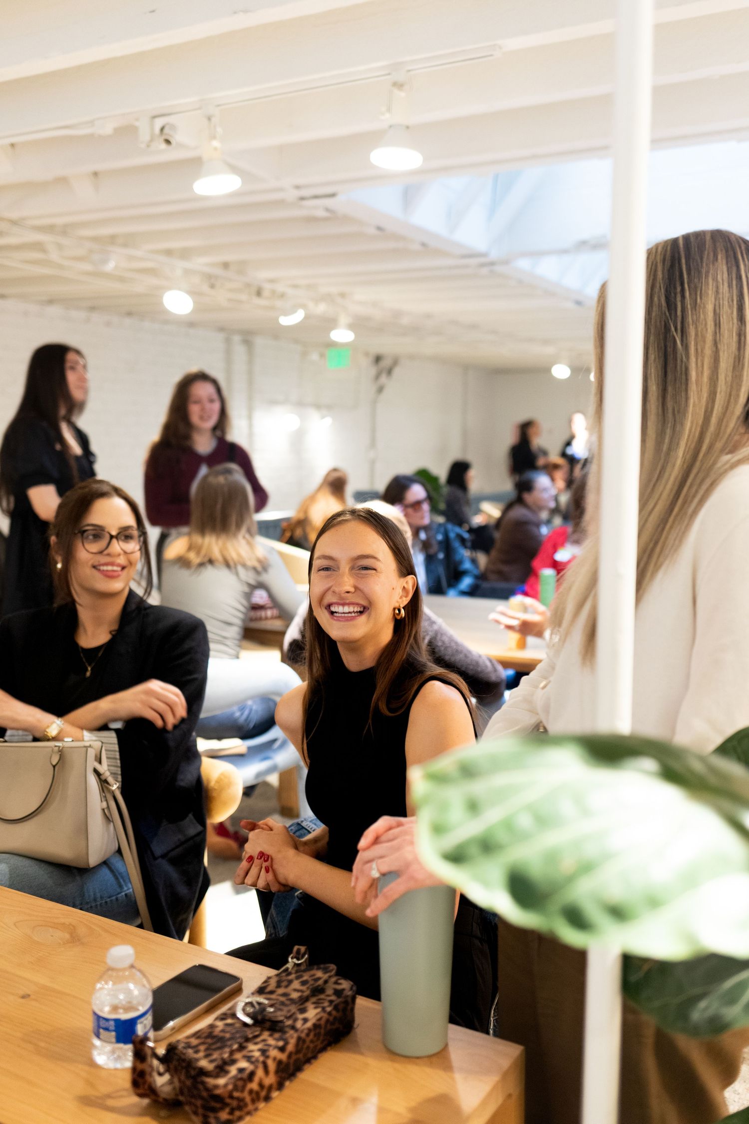 Women laughing and socializing at an indoor networking event with tables and warm lighting.