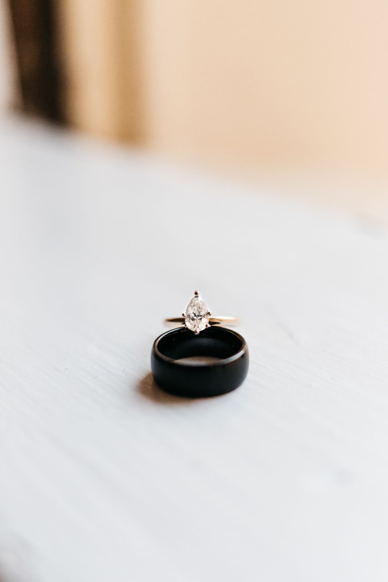 Gold engagement ring with marquise diamond resting inside a black wedding band on white surface.