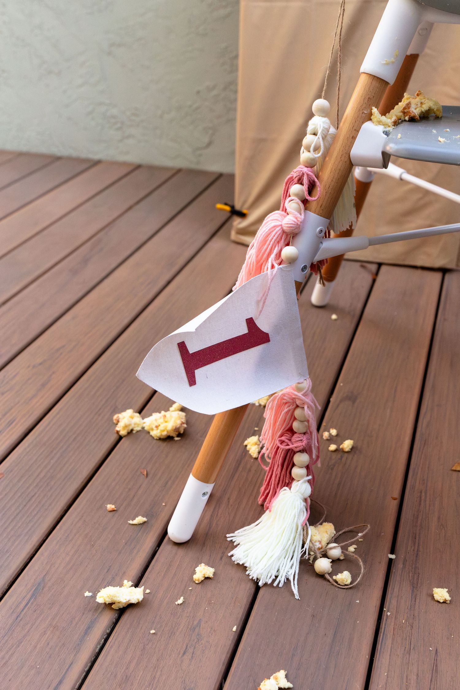 Handmade hobby horse toy with pink tassels and letter I flag on wooden deck with scattered popcorn.