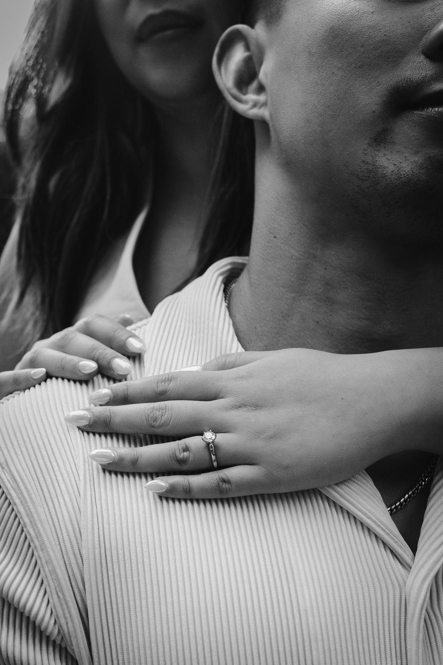 Black and white photo of a couple embracing, woman's hand with engagement ring resting on man's chest.