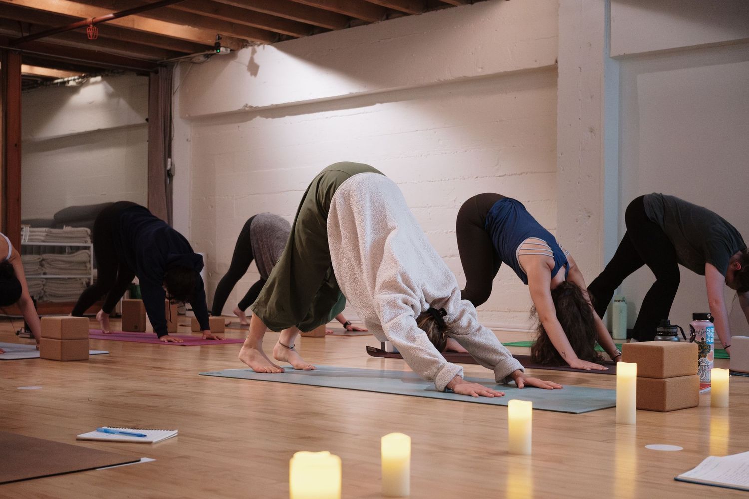 Group yoga class in downward dog pose on mats with candles in a serene studio.