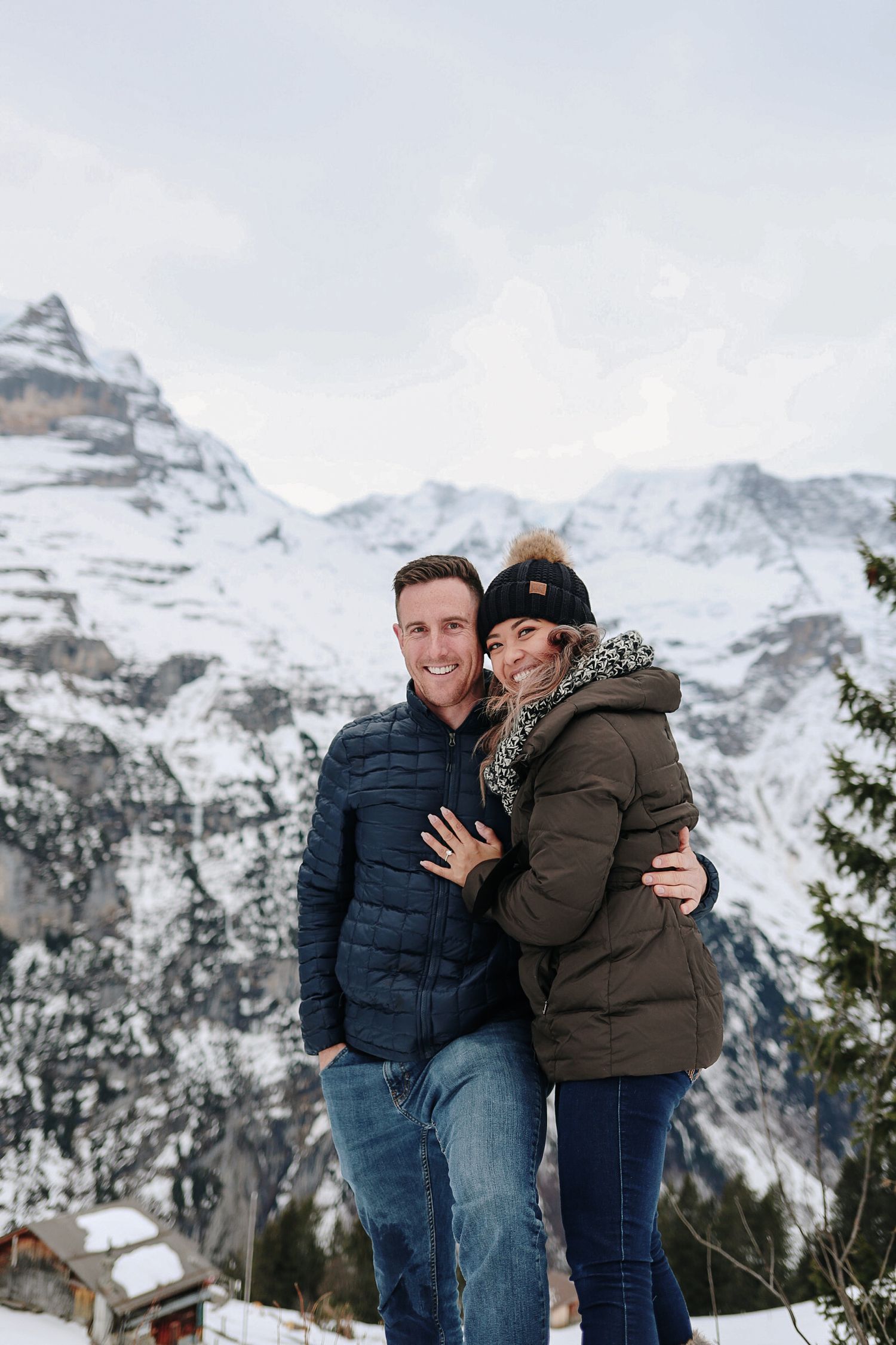Happy couple embraces and smiles together against a stunning snowy alpine mountain backdrop.