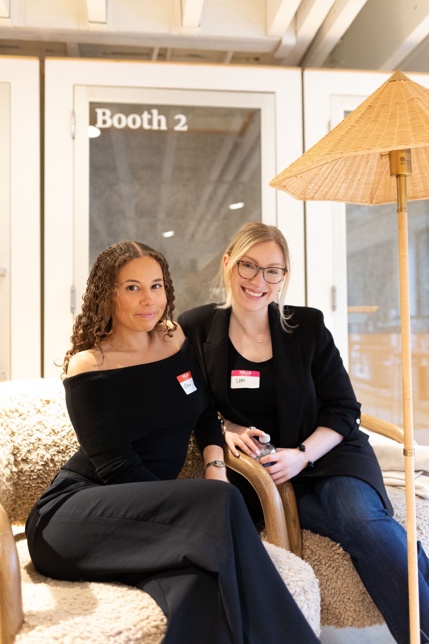 Two women wearing name tags smile while seated at a professional networking event near Booth 2.