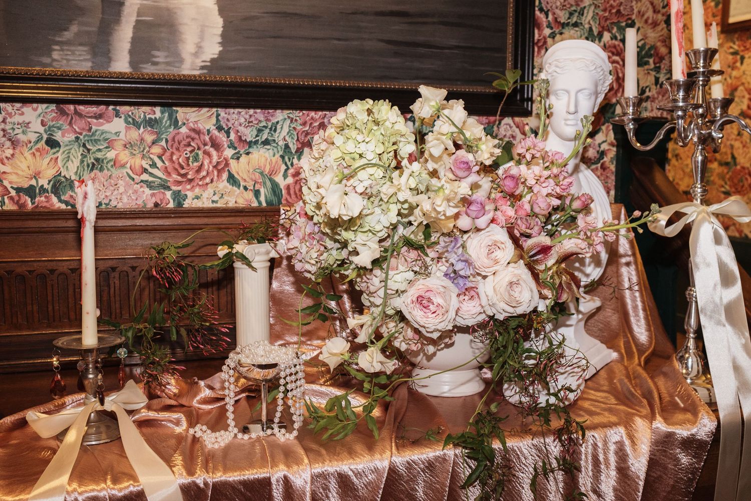 Elegant floral arrangement with pink roses and white hydrangeas beside a bust sculpture on a satin-draped table.