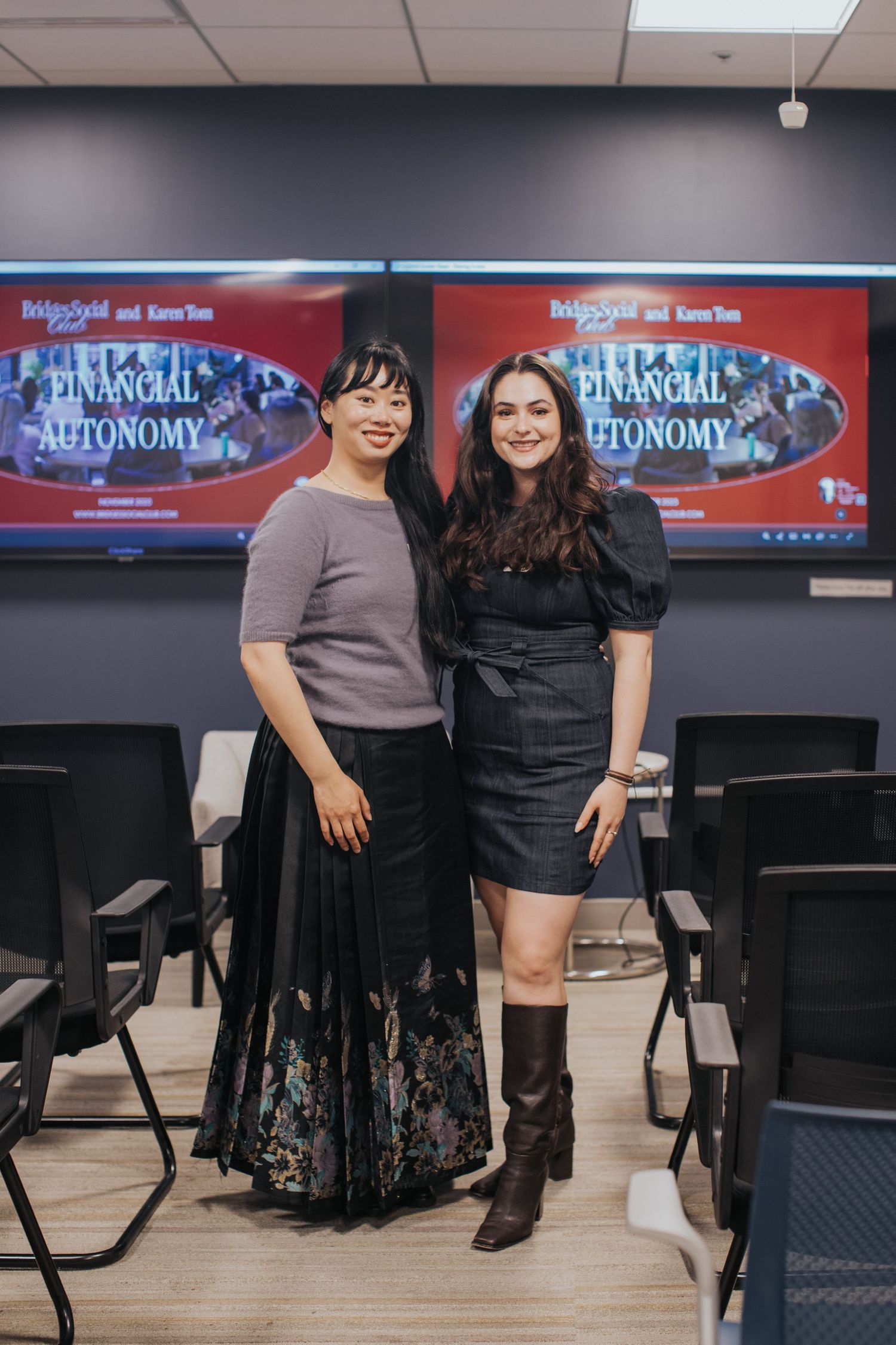 Two women pose together in front of Financial Autonomy presentation screens in a modern conference room.