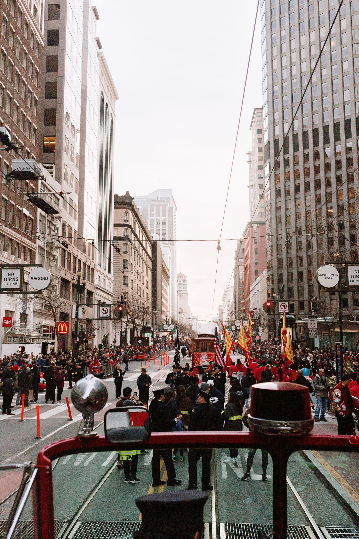 Aerial view of a city parade down a crowded urban street flanked by tall buildings and spectators.