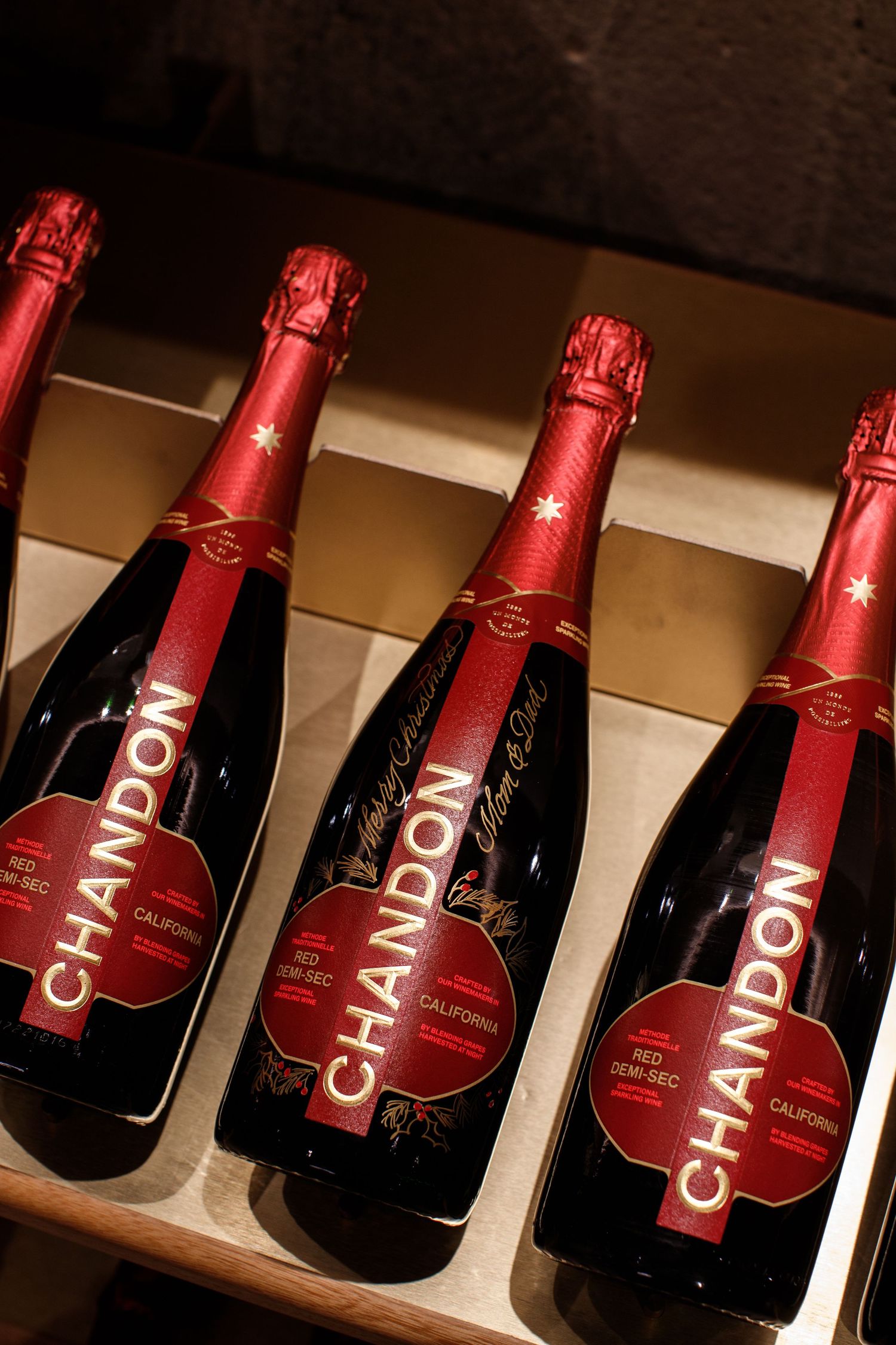 Four bottles of Chandon Red Demi-Sec California sparkling wine with red foil tops displayed on a wooden shelf.