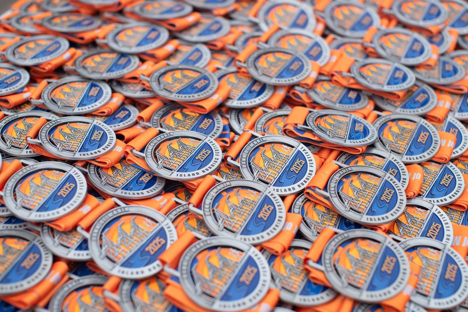 Pile of blue and orange marathon finisher medals with orange ribbons displayed at a racing event.