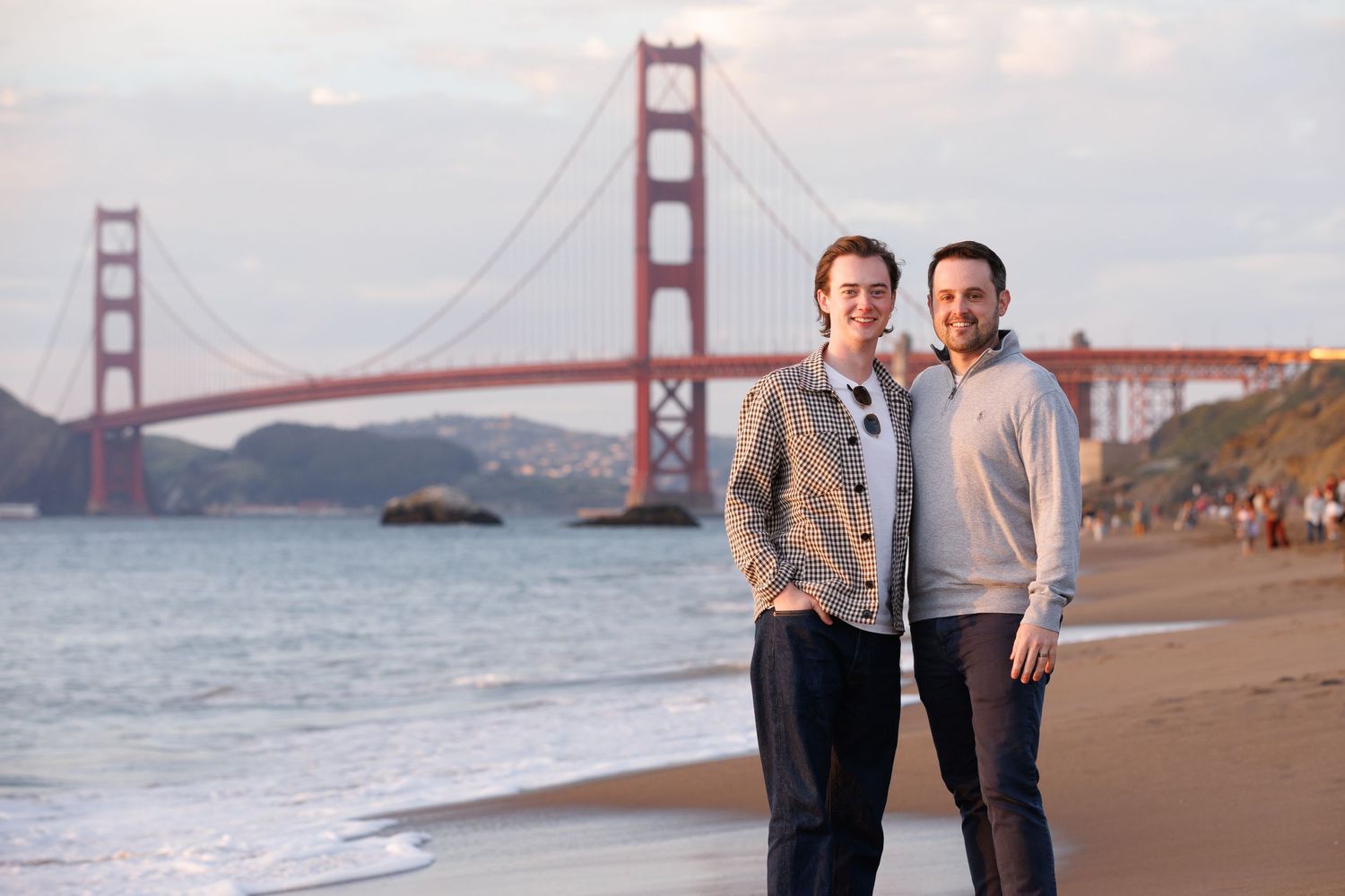 Couple smiling on Baker Beach with the Golden Gate Bridge in the background at sunset in San Francisco.