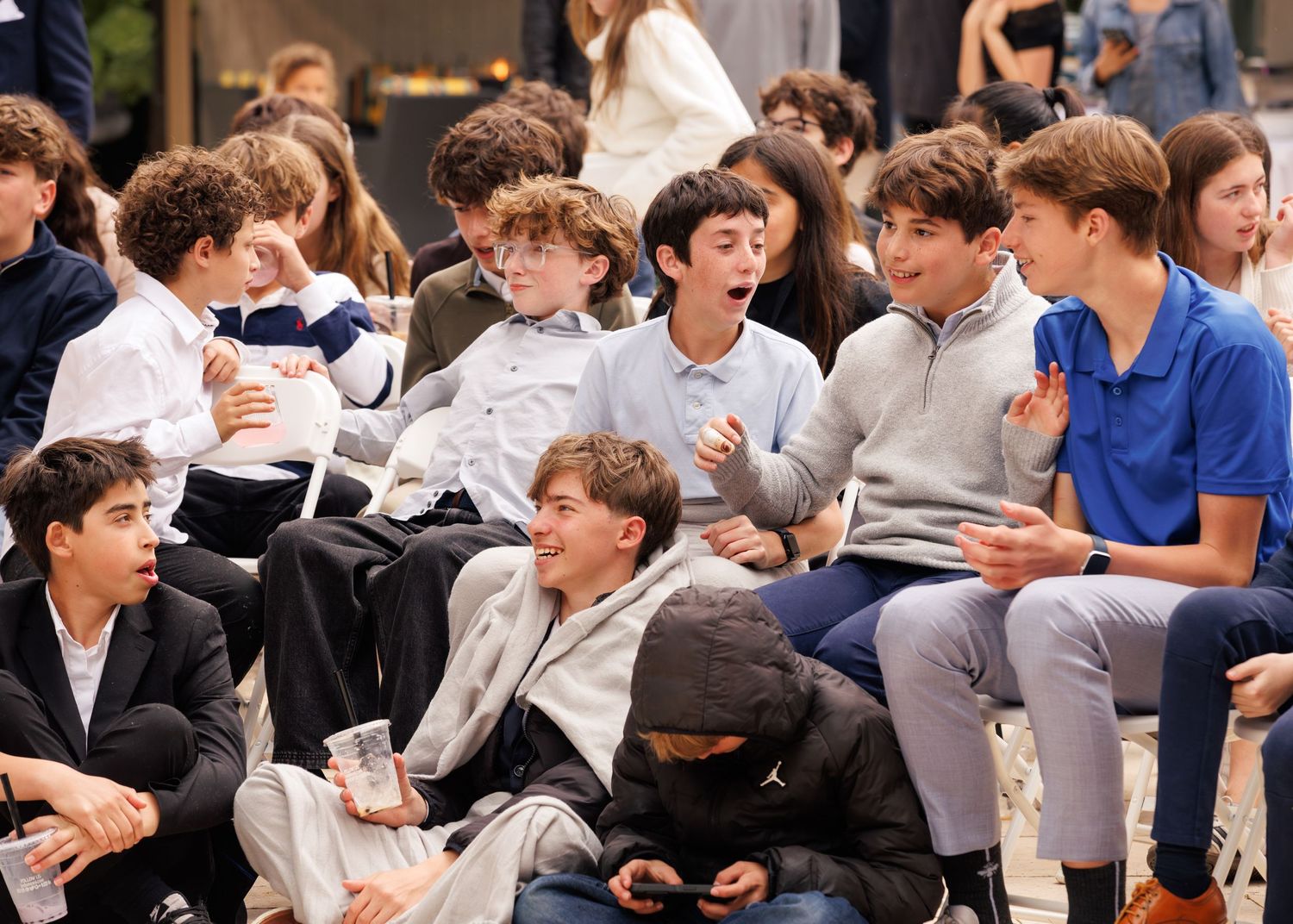 Group of young teenage boys laughing and reacting expressively while seated together at an indoor event.