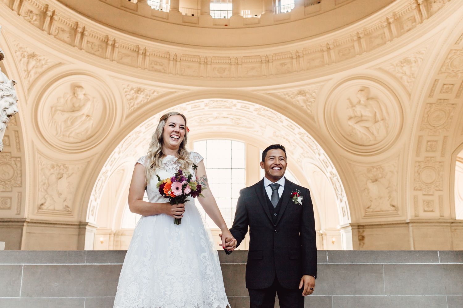 Bride and groom holding hands under ornate arch at San Francisco City Hall wedding ceremony.