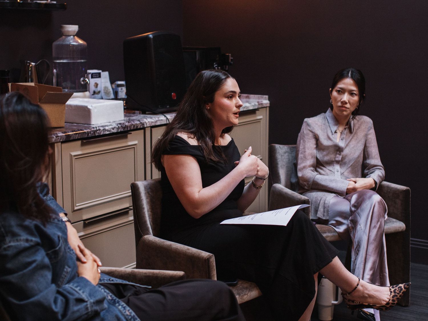 Three women seated in chairs during a panel discussion in a modern interior setting.