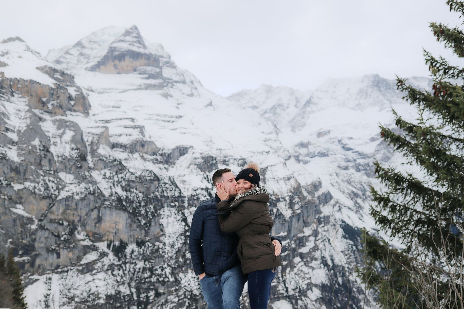 Couple shares a romantic kiss with snow-covered Swiss Alps mountains in the background.