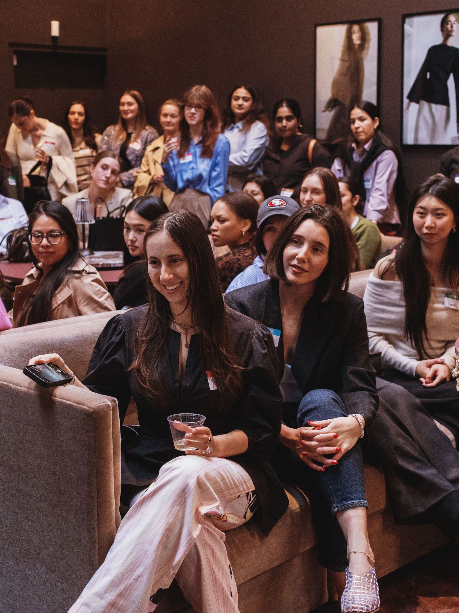 A diverse group of women seated in a modern venue, smiling and engaged at a fashion or networking event.