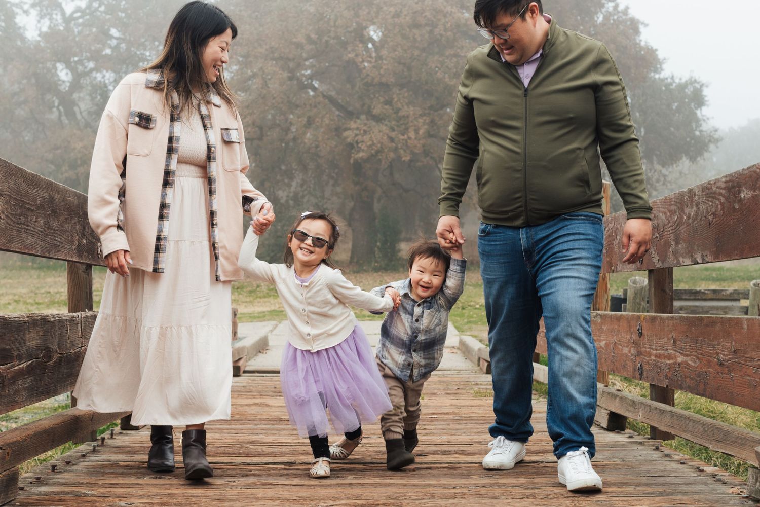 Family walking together on a foggy autumn day holding hands on a brick pathway in matching outfits.