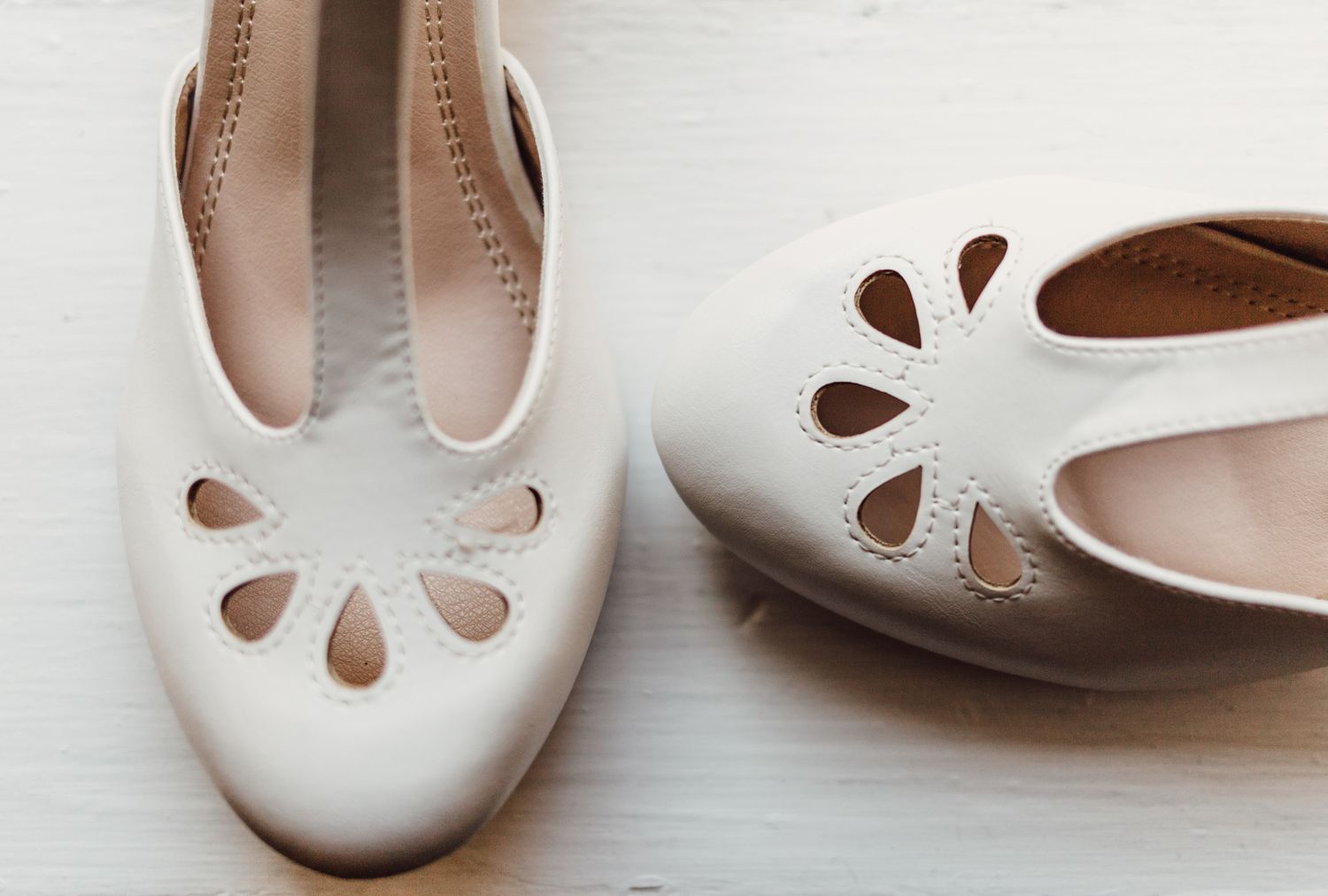 Elegant white leather ballet flats with decorative cutout floral details, displayed on a light wooden surface.