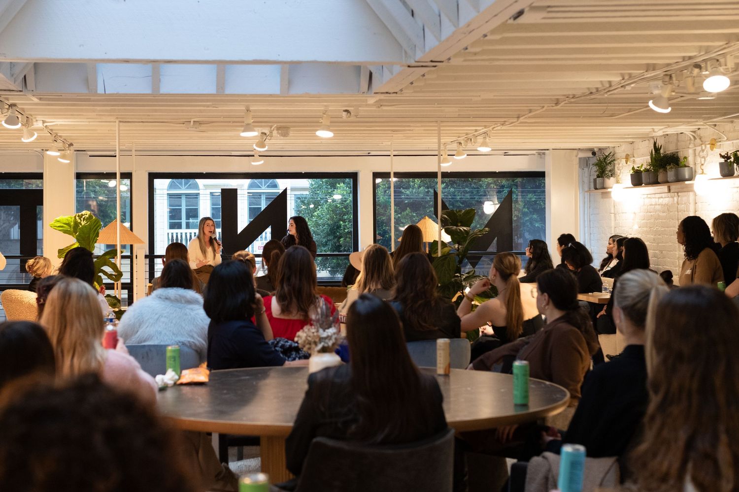 A diverse group of women attend an indoor professional networking event in a modern bright office space.