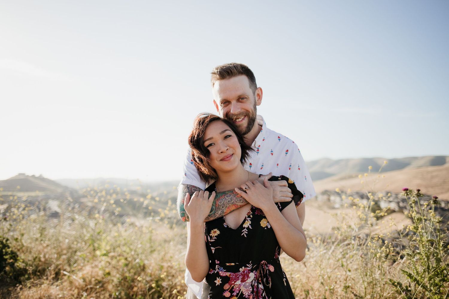 Couple embracing on a sunny hilltop with rolling golden hills and blue sky in the background  in Dublin, California.
