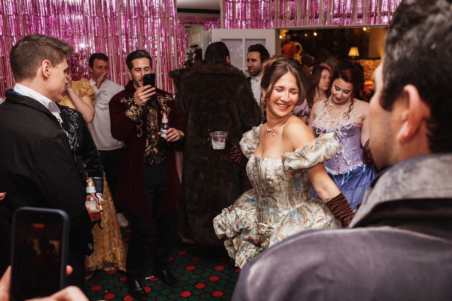 Woman in ornate historical costume dancing at a festive costume party with guests in formal attire.