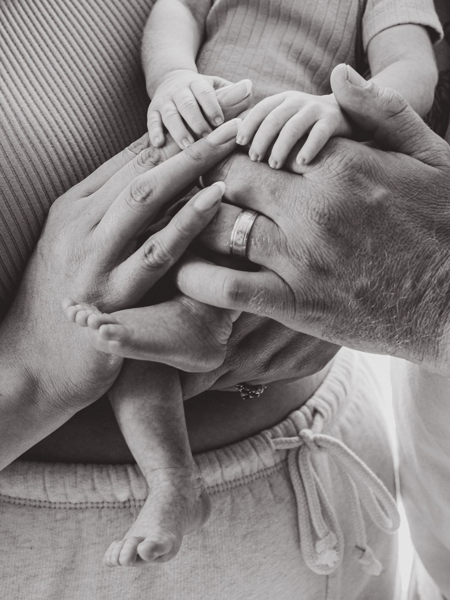 Black and white photo of adult hands and a newborn baby's tiny feet and hands together, symbolizing family love.