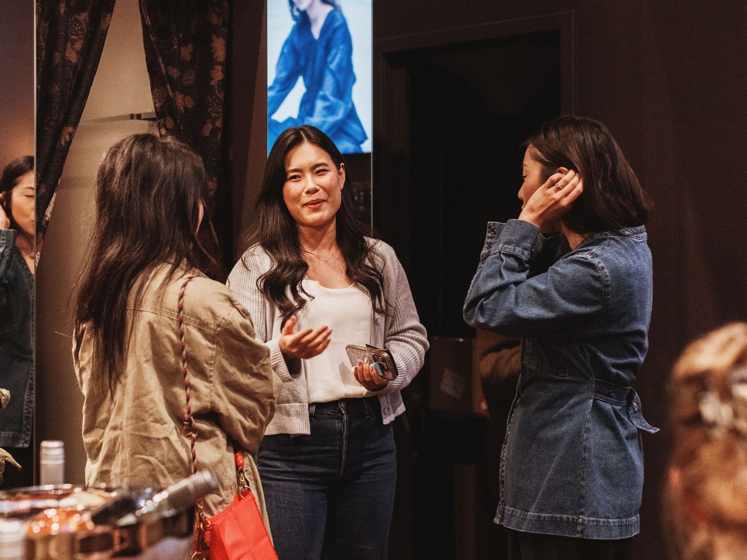 Three women engaged in conversation at an indoor networking event, with soft lighting and decor in the background.
