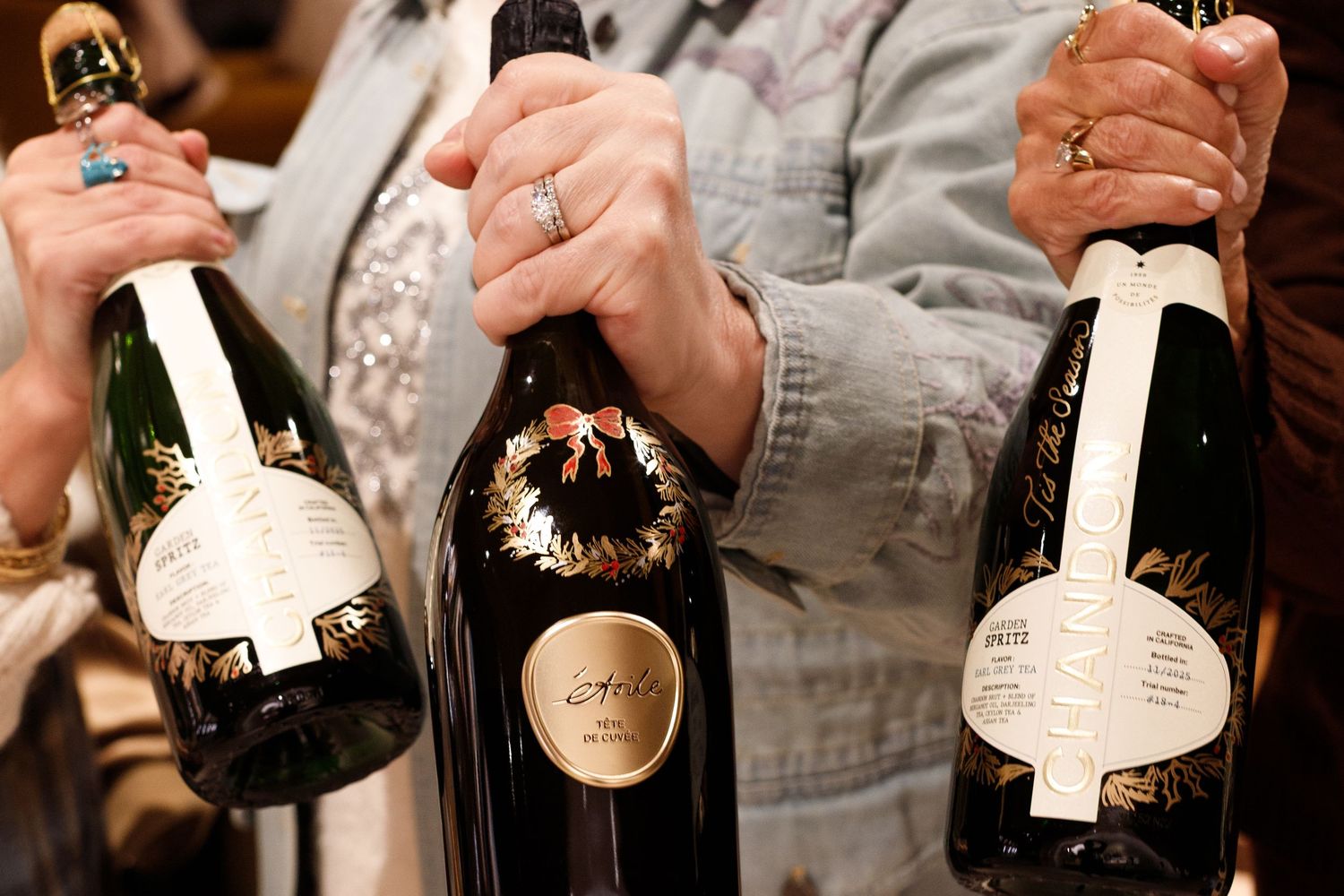 Three elegant champagne bottles held by people at a wine tasting event, featuring decorative labels.