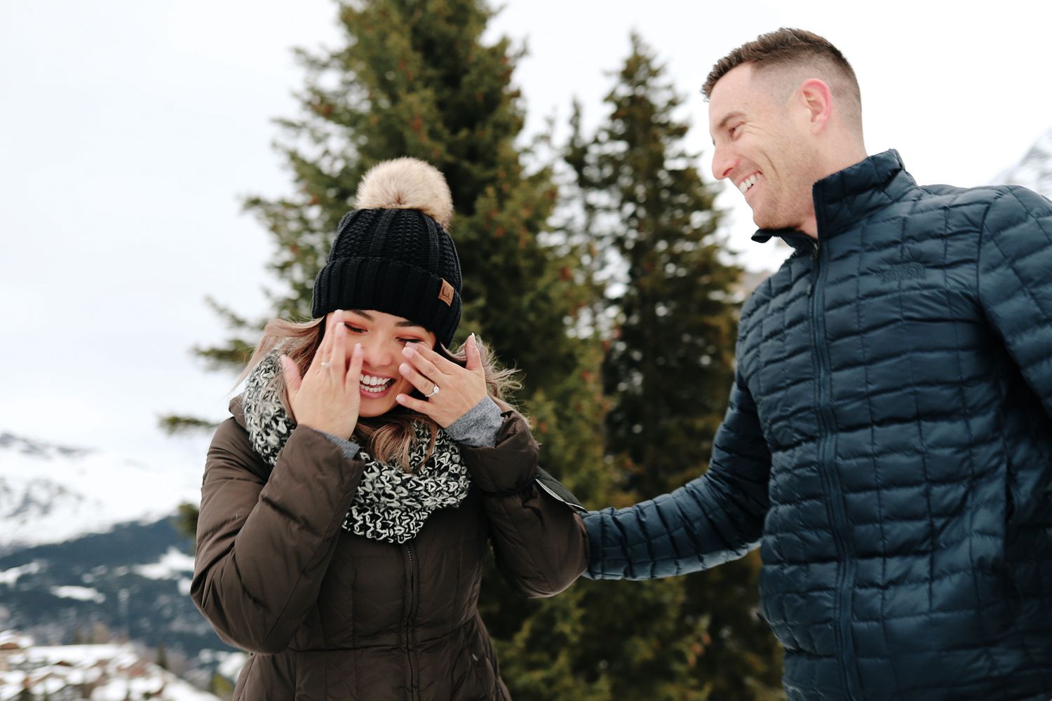 Couple sharing emotional marriage proposal moment in snowy mountain winter landscape.