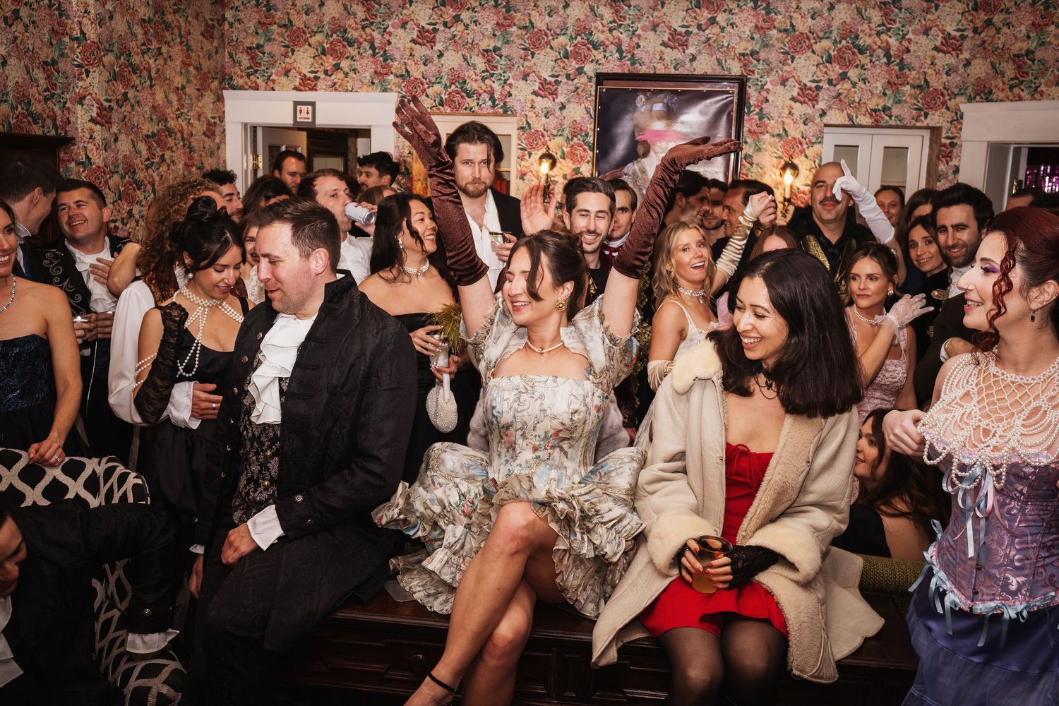 Lively party scene with elegantly dressed guests socializing and laughing in a decorated room.