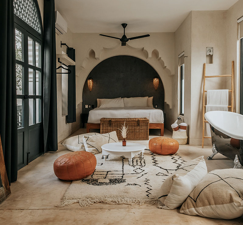 Modern boho bedroom with arched alcove bed, leather poufs, black accent wall and decorative rugs in neutral tones.