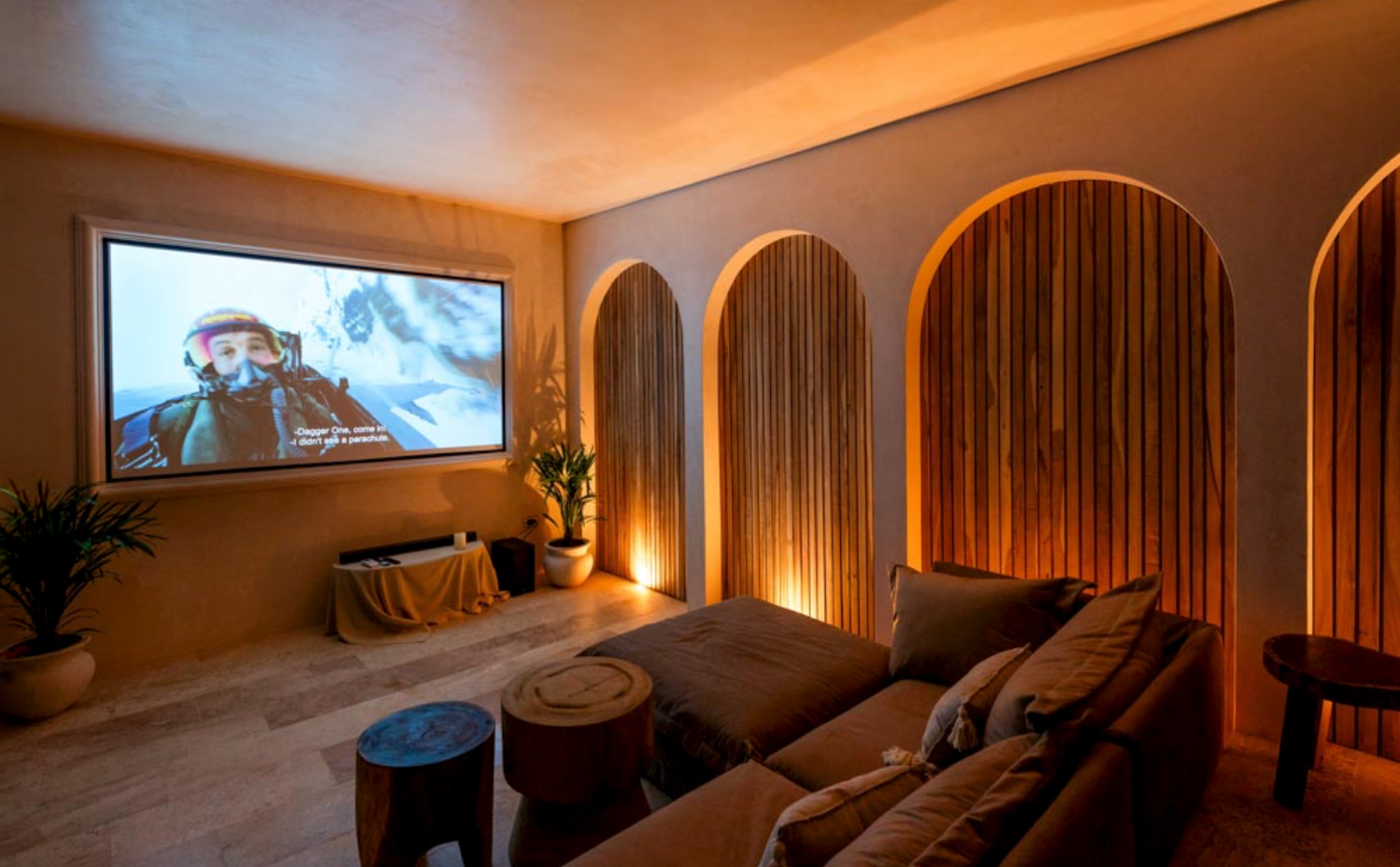 A cozy home theater room with wood arch panels, ambient lighting, and a large projector screen showing a movie.