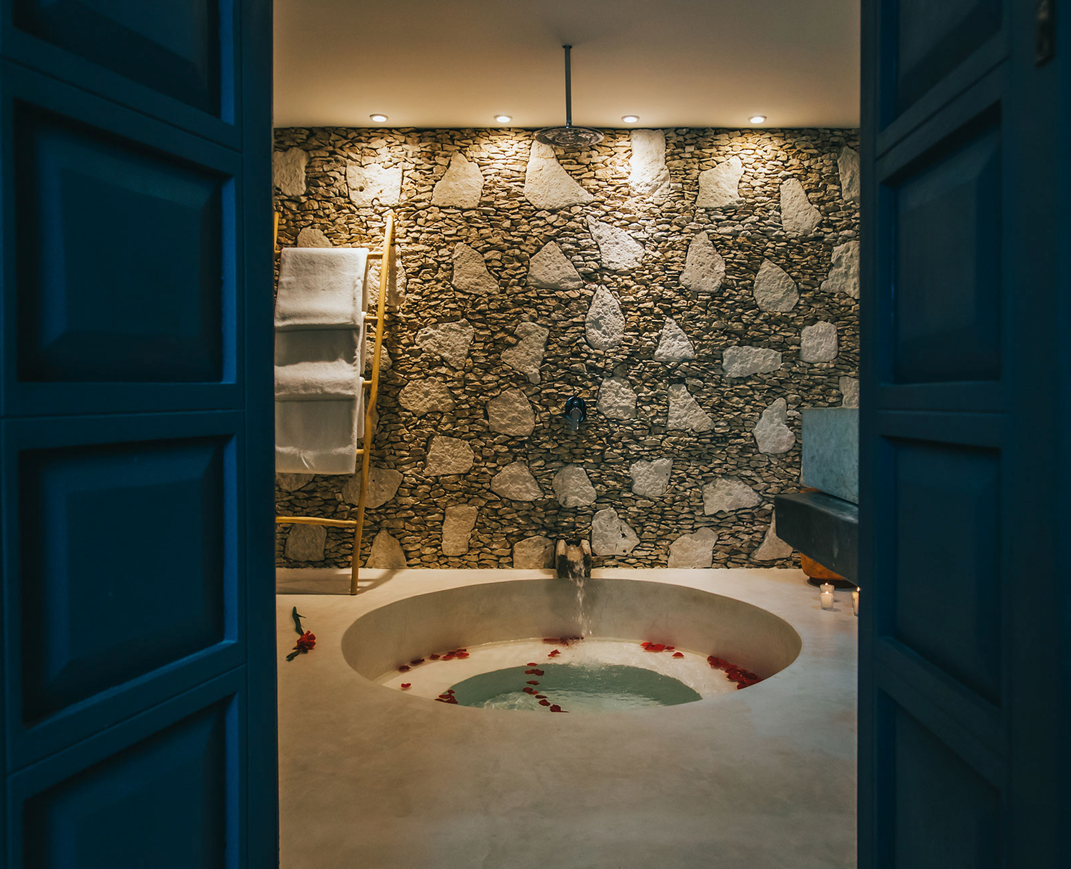 Rustic stone wall adds texture to modern basement interior with recessed lighting and gray floor tiles.