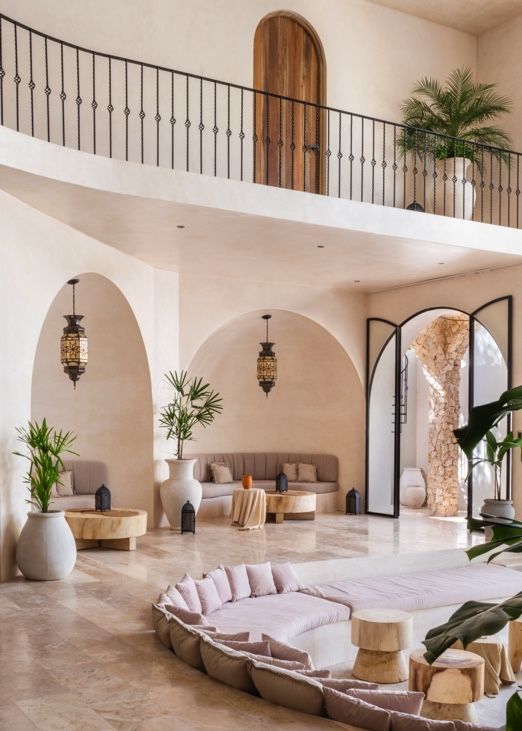 Luxurious Mediterranean-style living room with curved sofa, arched doorways, and potted palms in an open-concept space.