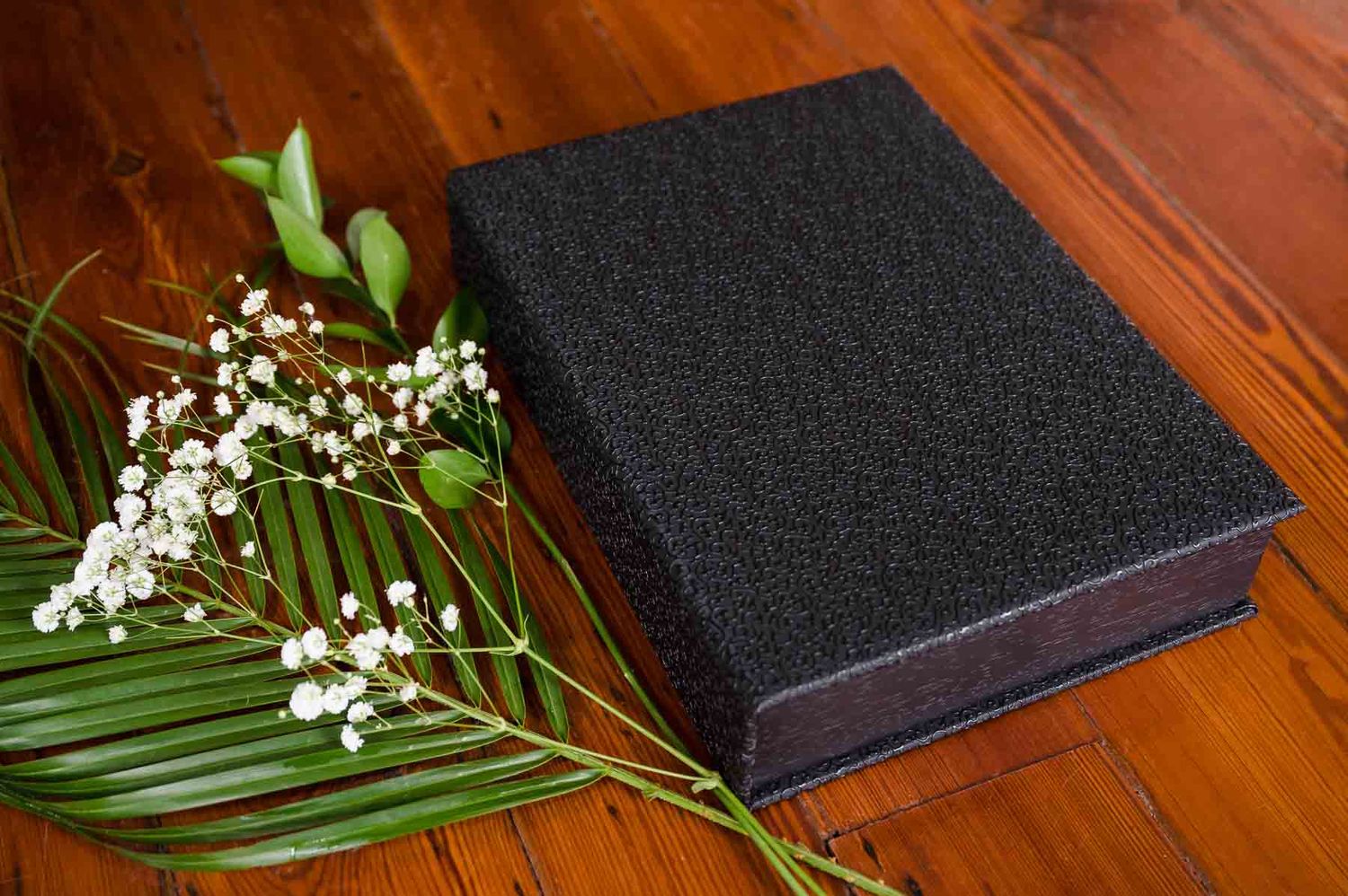 Elegant black box with textured surface decorated with palm leaves and white flowers.