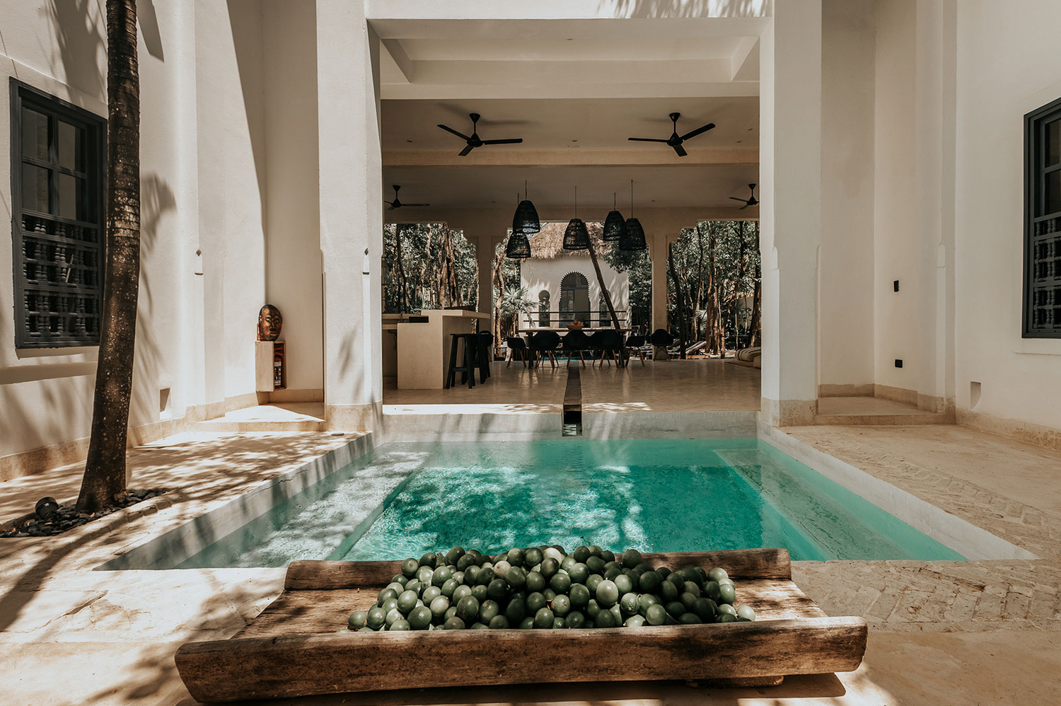 Sunlight streams through windows into a modern indoor swimming pool with dark wood accents and sleek stone floors.