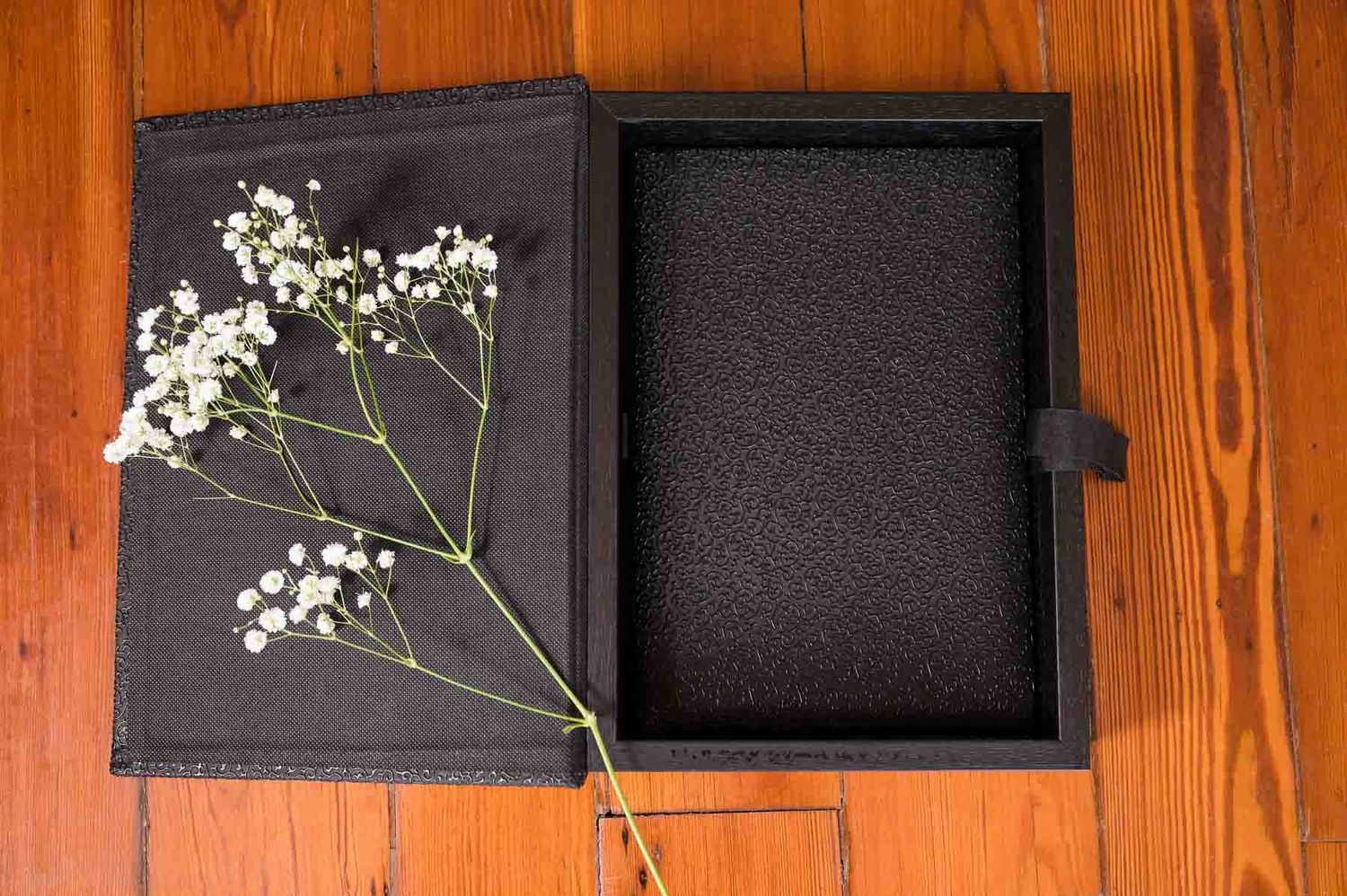 Open black box with foam padding interior and baby's breath flowers against wooden background.