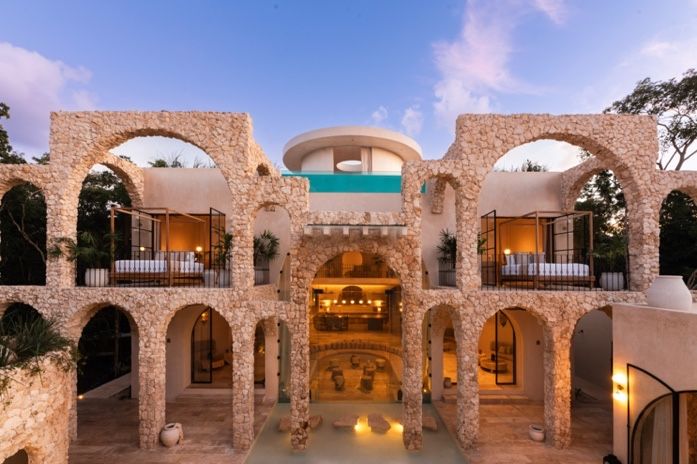 Stone arches and columns illuminate a rustic Mediterranean courtyard venue at sunset with warm glowing lights.