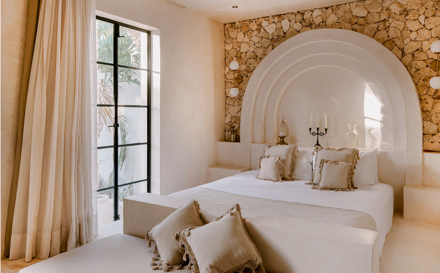 Elegant Mediterranean-style bedroom with stone walls, arched doorways, and white bedding in a luxury villa.