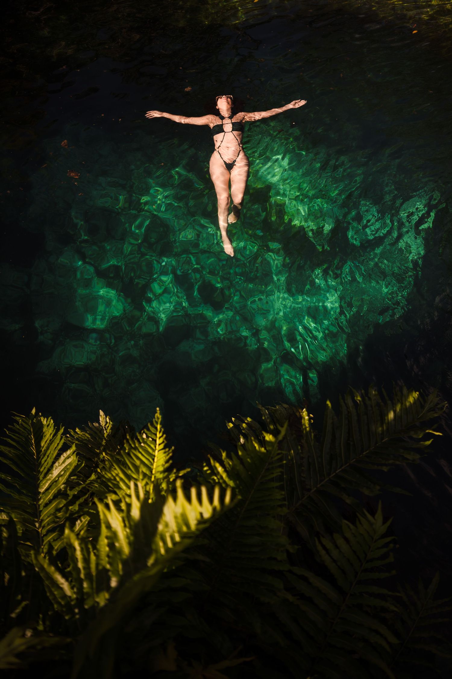 A swimmer floats gracefully in emerald green cenote waters, surrounded by tropical ferns in Mexico.