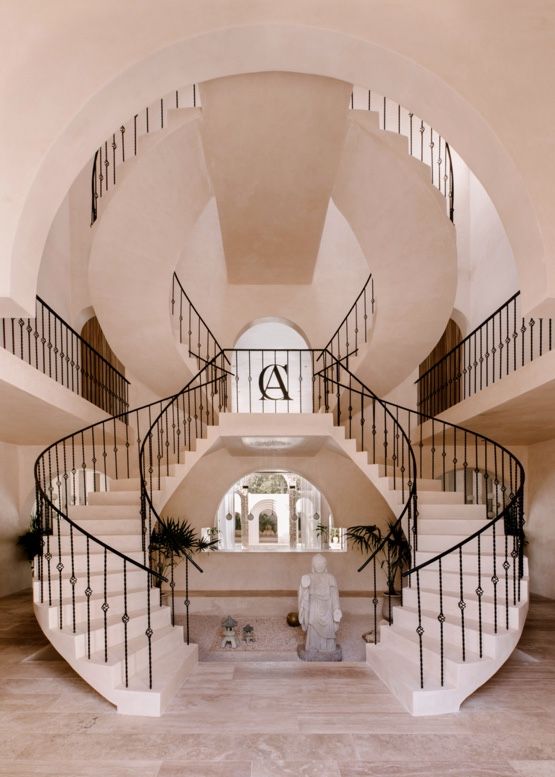 Elegant curved staircase with wrought iron railings and arched design in a luxurious white interior setting.