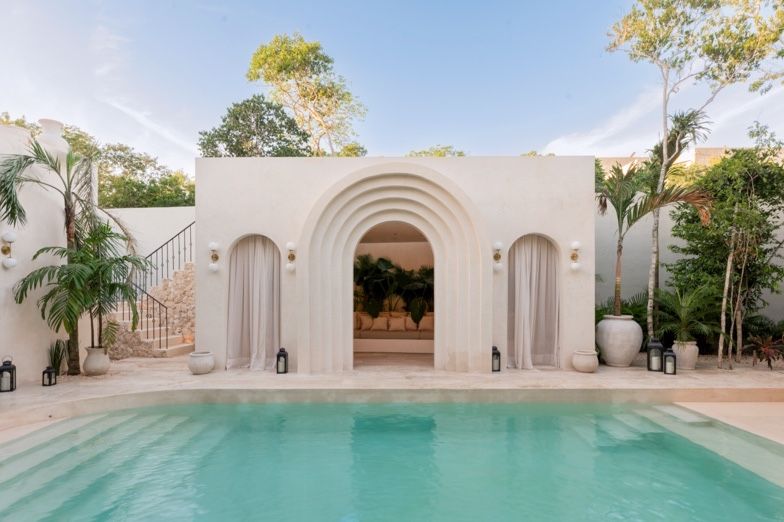 A luxurious white Mediterranean-style pool area with arched columns and palm trees creating an elegant outdoor oasis.