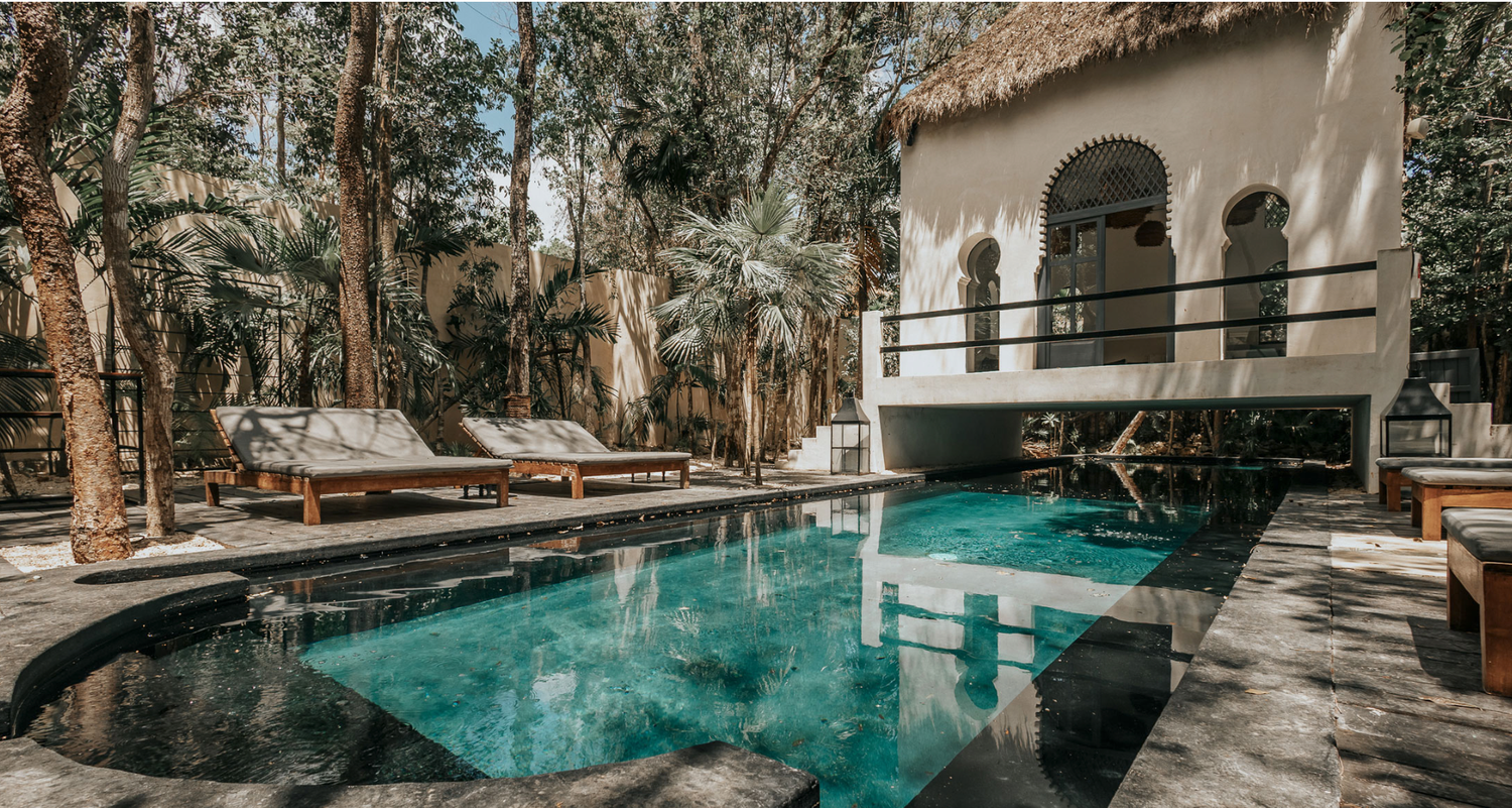 Luxurious swimming pool surrounded by lounge chairs and Spanish-style architecture nestled in a wooded setting.