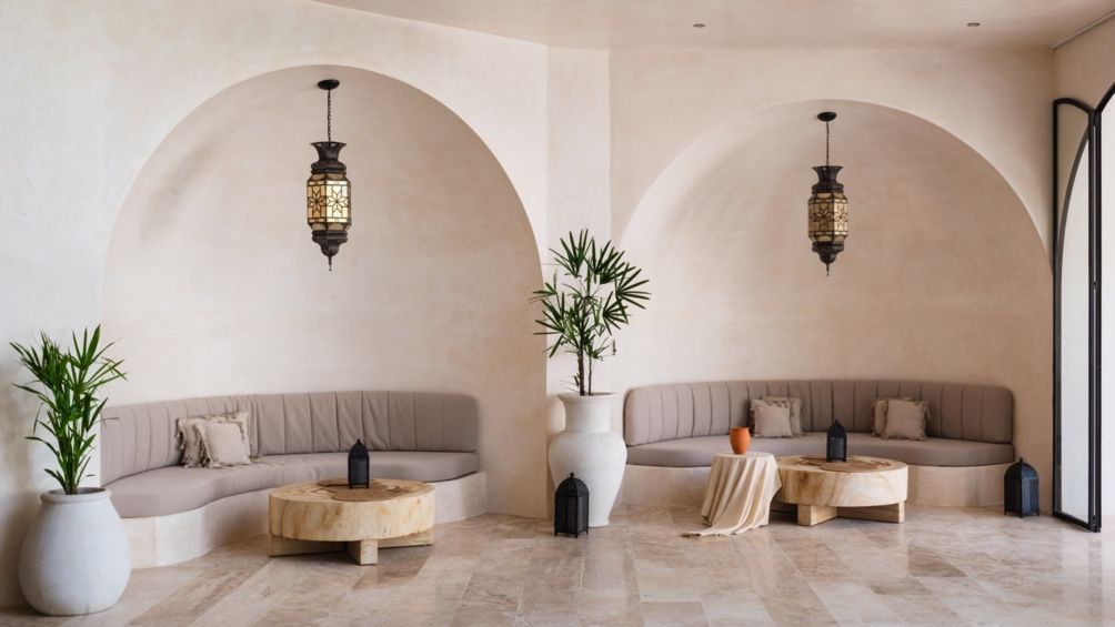 Modern curved archways lead into a minimalist interior space with neutral tones and potted plants as decor elements.