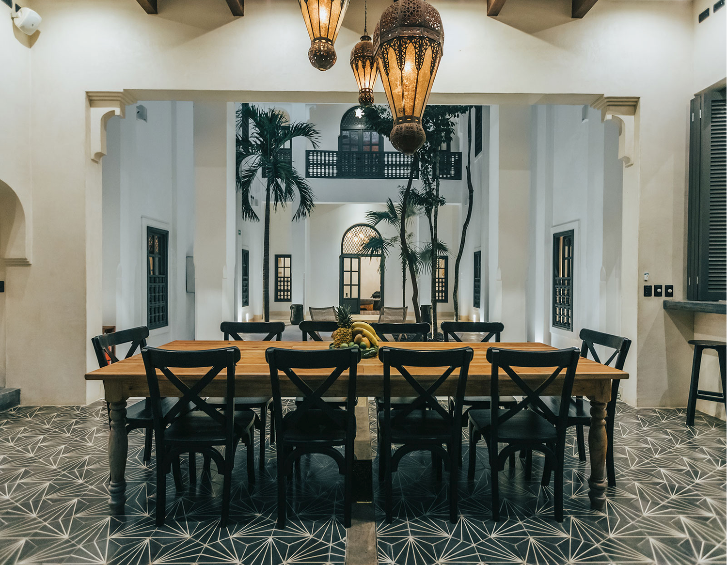 A rustic dining room interior with exposed wooden beams, stone walls, and elegant pendant lighting fixtures.