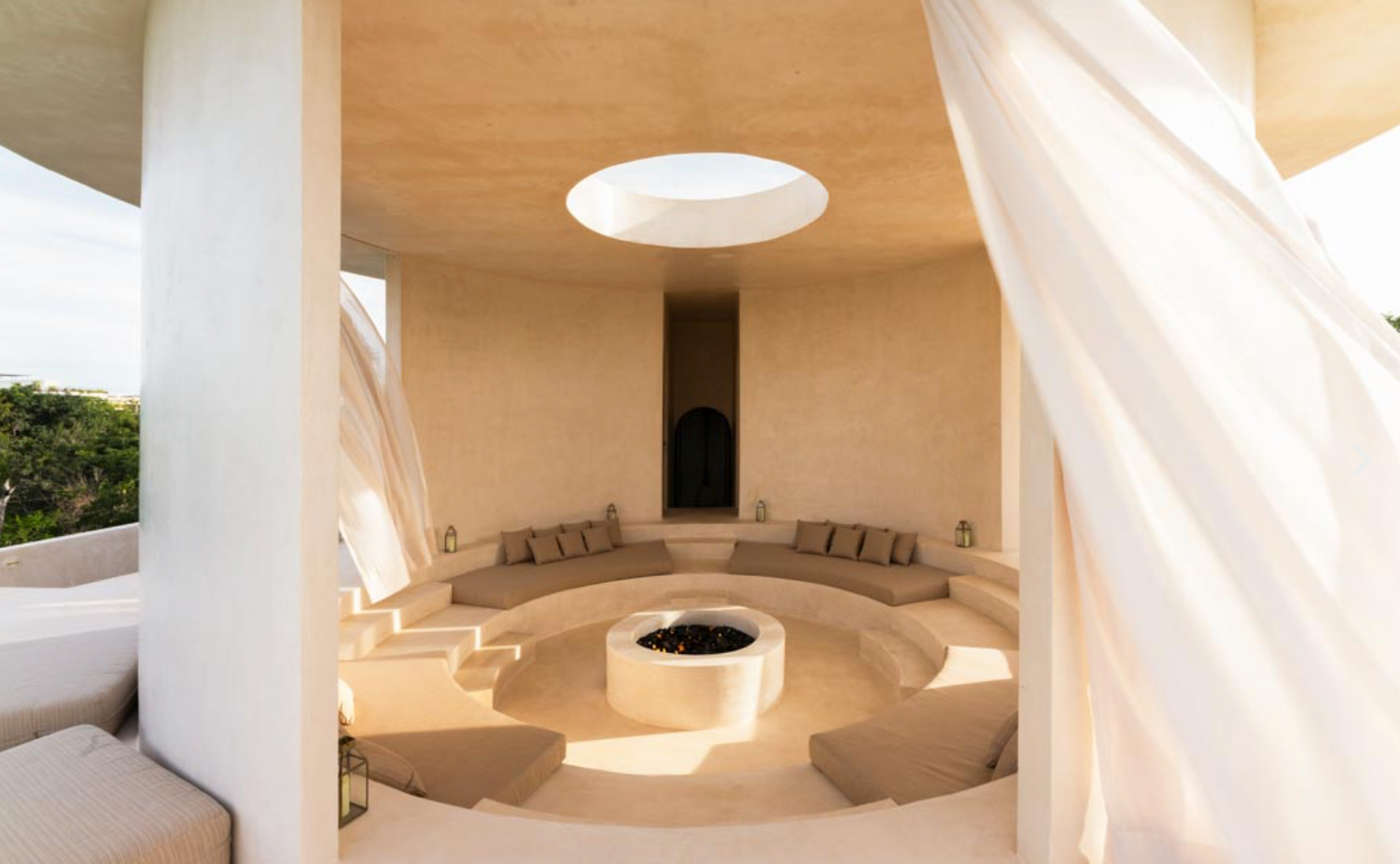 Minimalist white interior space with curved walls and circular skylight creating soft natural illumination.