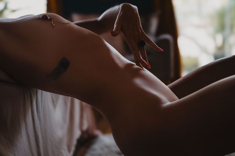 Close-up silhouette of a person on a bed in soft natural light creating an intimate artistic atmosphere.