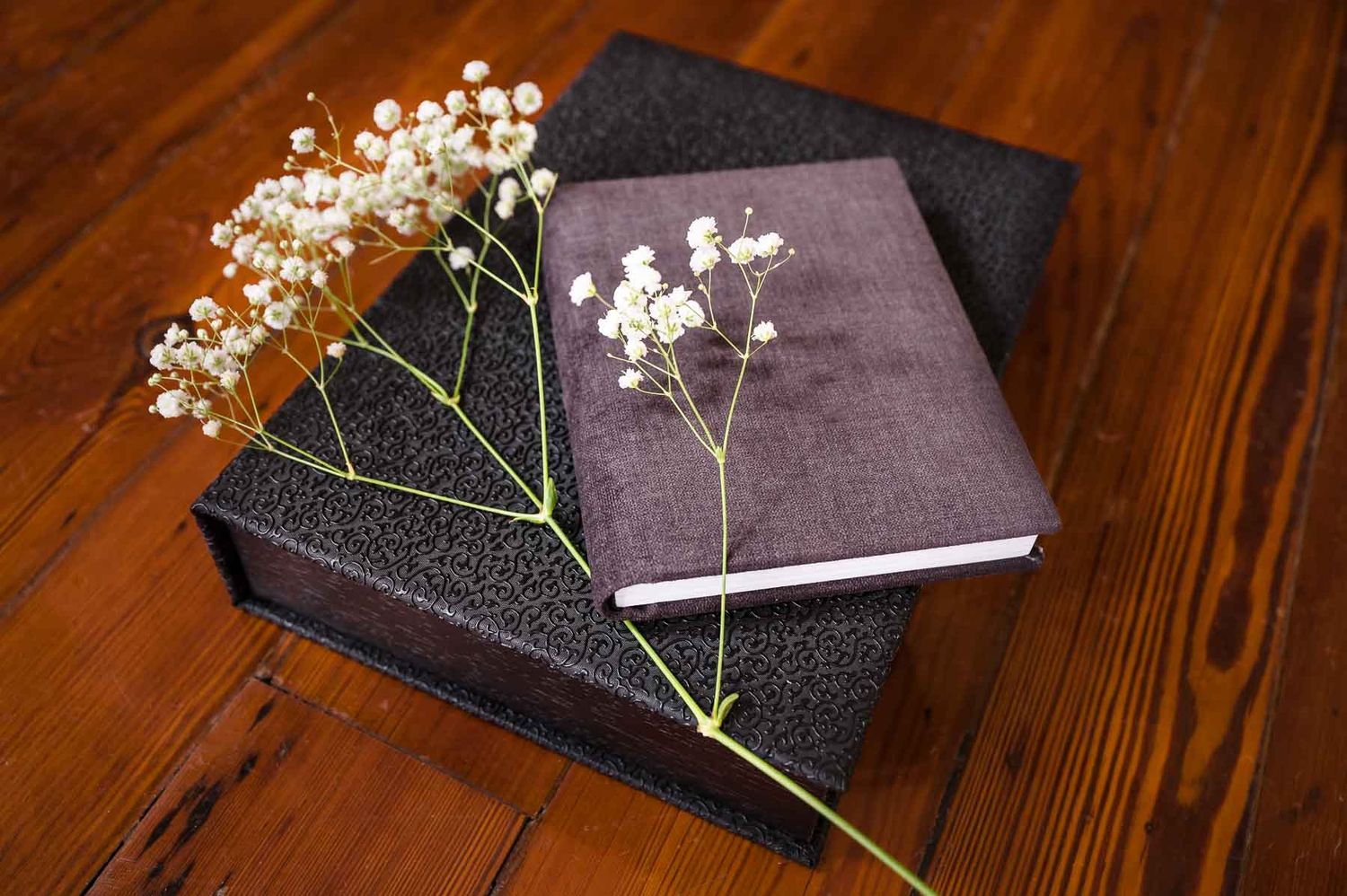Black photo albums decorated with sprigs of baby's breath flowers on rustic wooden surface.