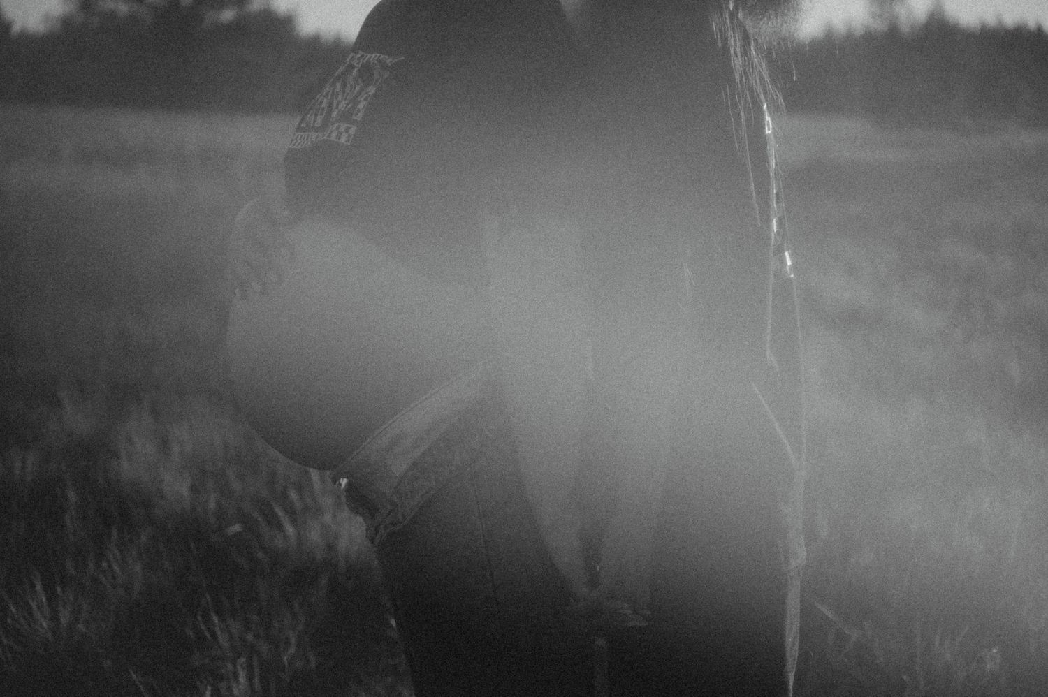 A silhouette against hazy light in a misty field creates a moody black and white atmospheric scene.