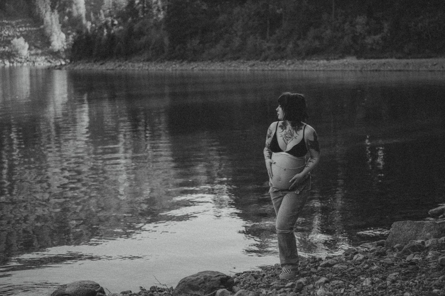 A person stands in shallow water near a rocky shore, photographed in dramatic black and white.