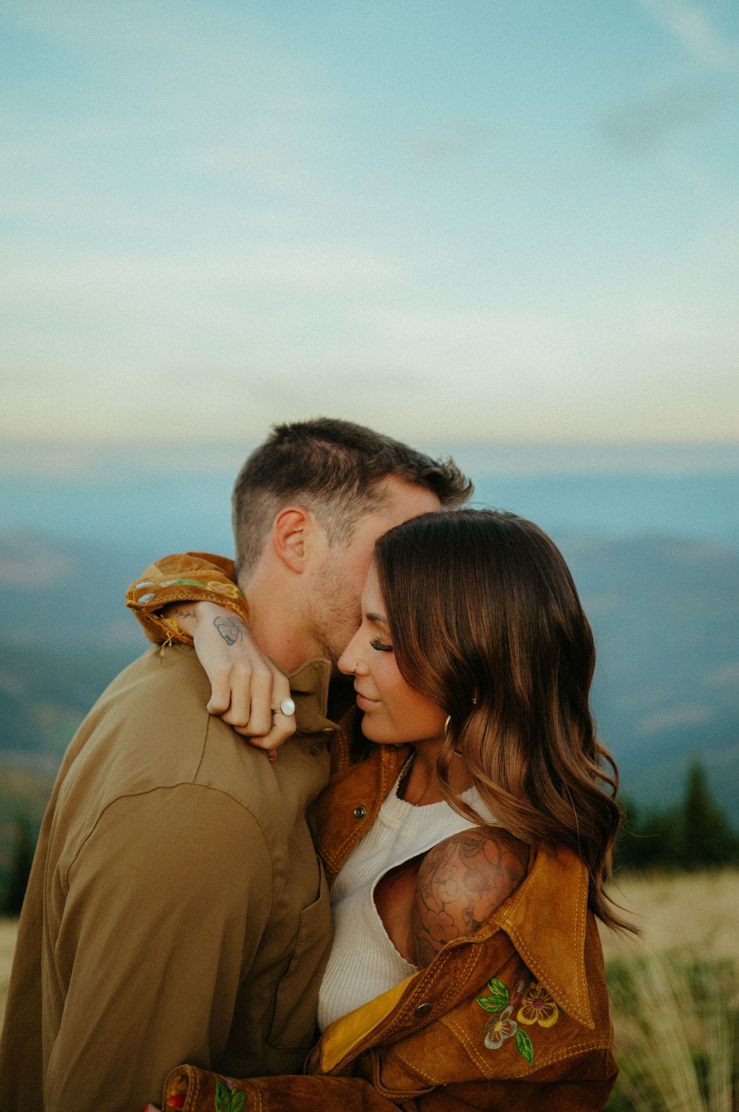 Romantic sunset portrait of an intimate couple embracing on a mountaintop with scenic views in the background.